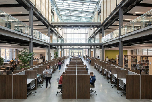 Modern library with high ceilings and large windows, people studying at desks.